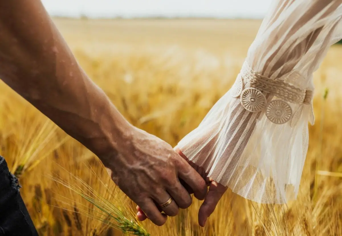 Romantic couple holding hands in a field. Close up shot of man and woman holding hands and walking through field. Man with vitiligo on hand.